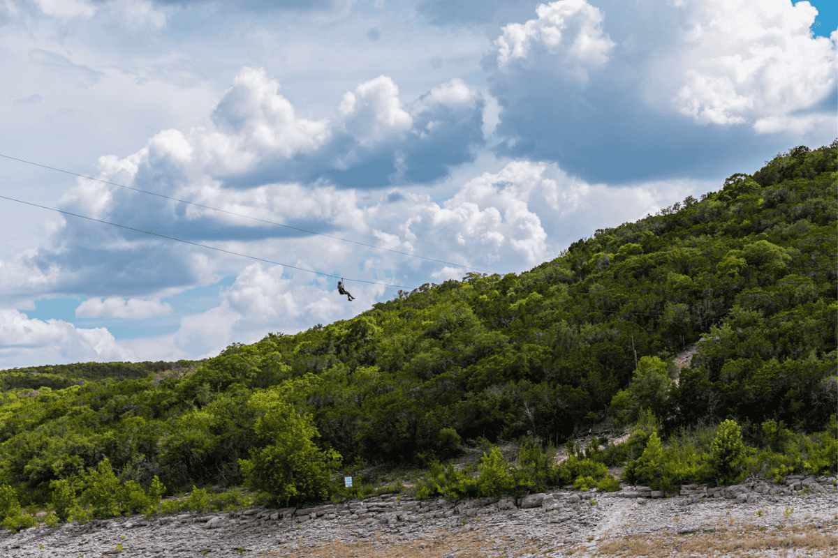 A person zips across a cable above a lush green hillside