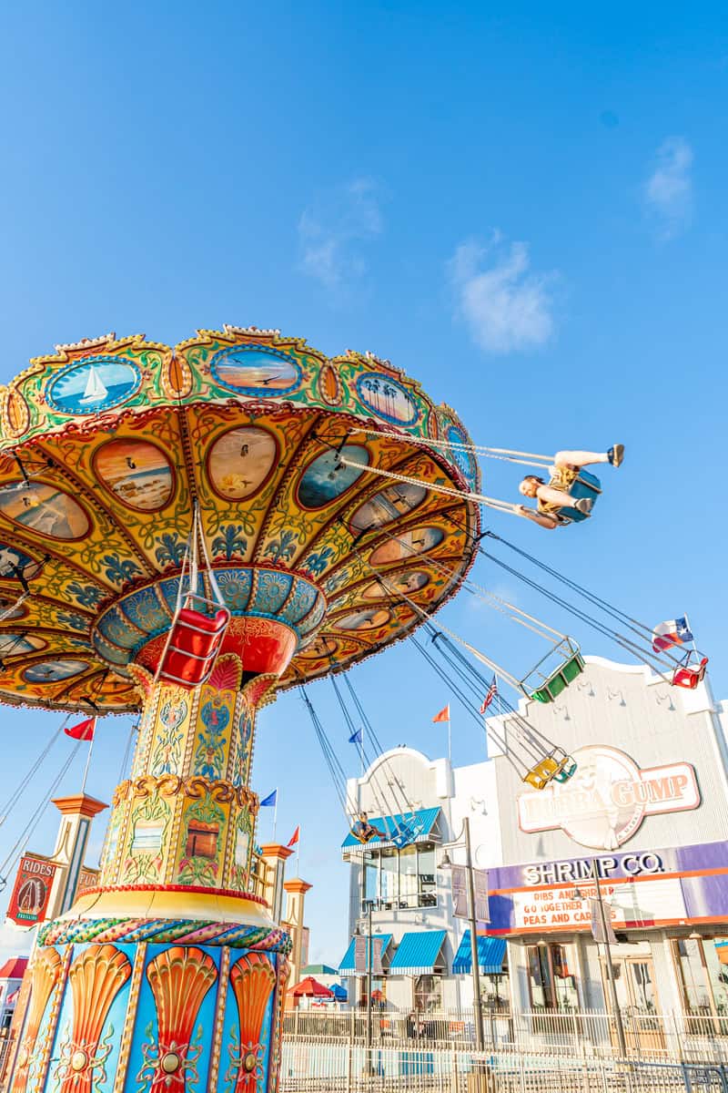 A vibrant swing ride with colorful designs spins against a clear blue sky