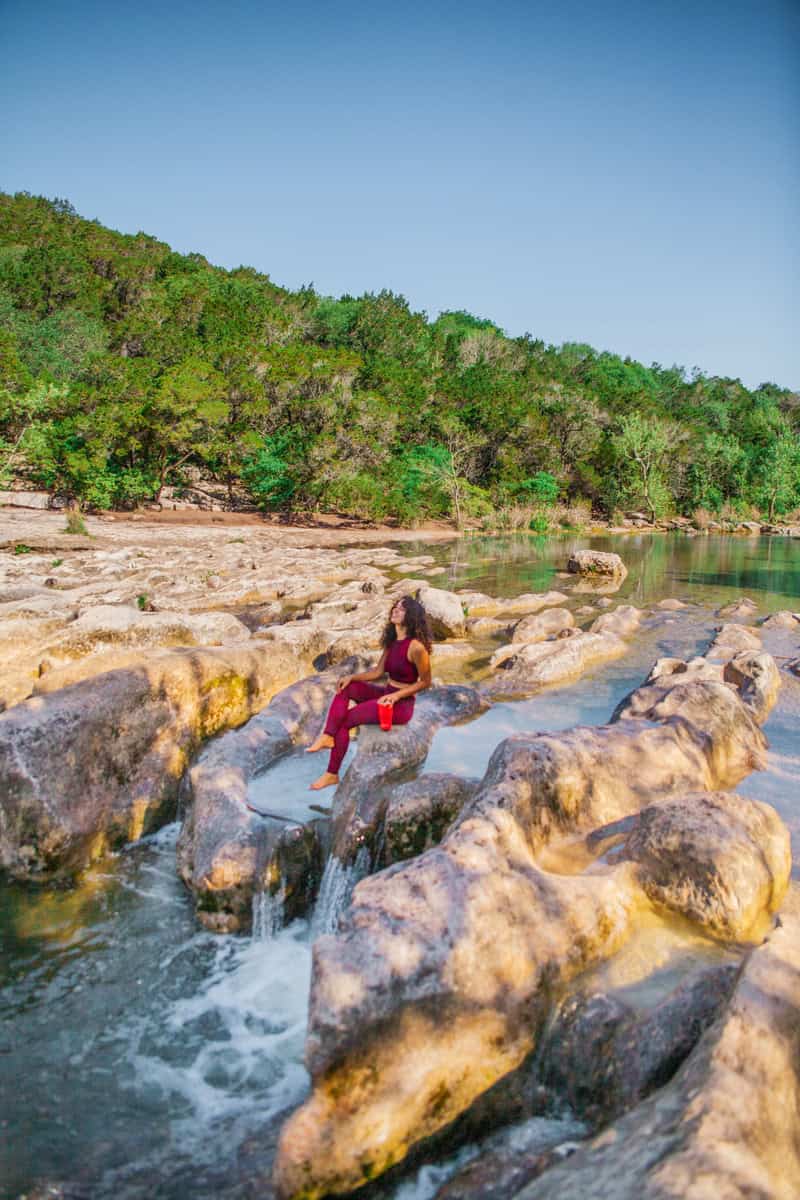 A woman in burgundy activewear sits on rocky ledges