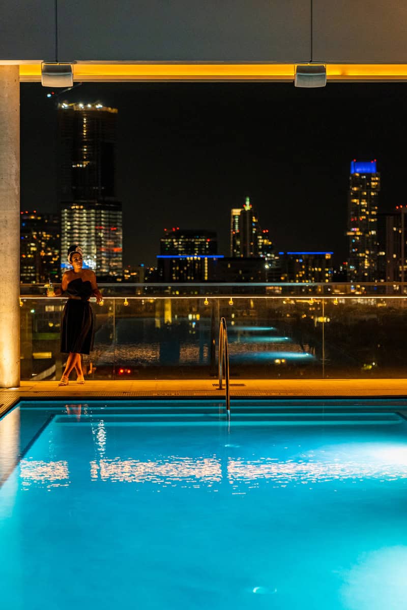 A woman in a black dress stands by a glowing pool