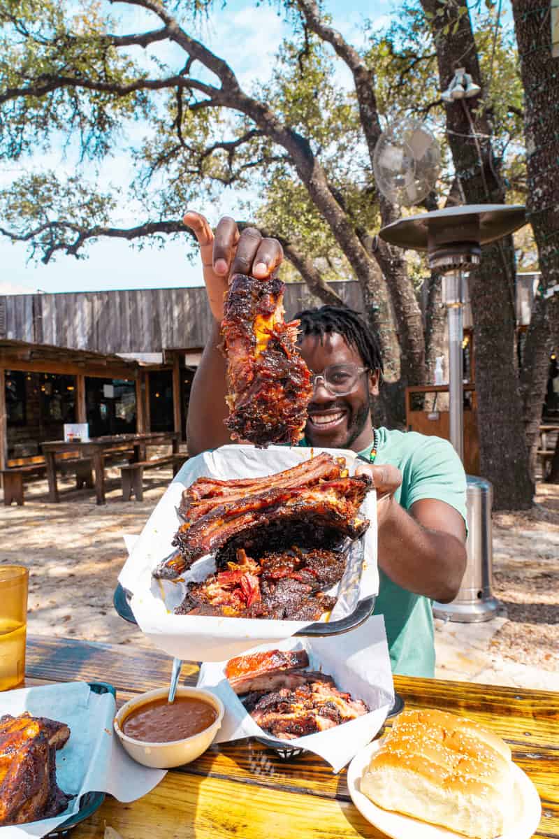 A person holds up a large, juicy rib above a table spread