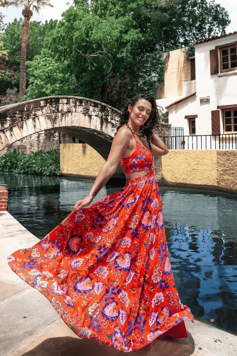 A woman twirls in a vibrant red floral dress by a serene canal