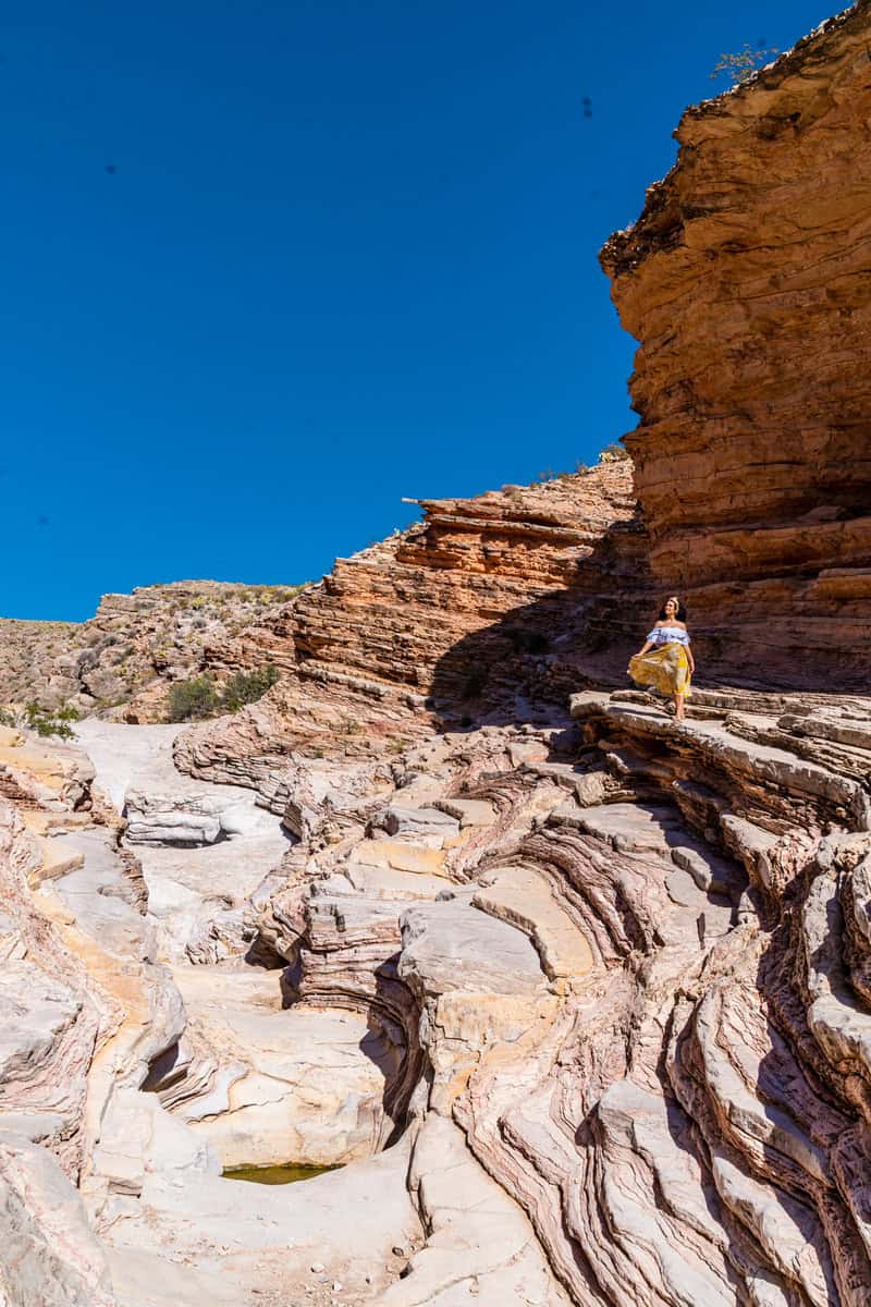 A woman in a yellow dress stands on layered sandstone rock formations