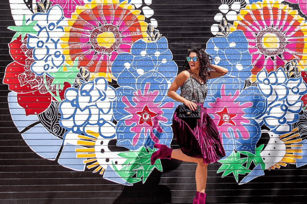 A stylish person poses playfully in front of a vibrant mural