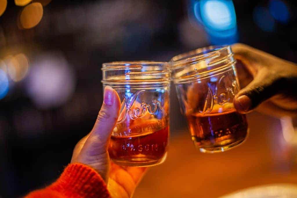 Two hands clink mason jars filled with a deep reddish drink