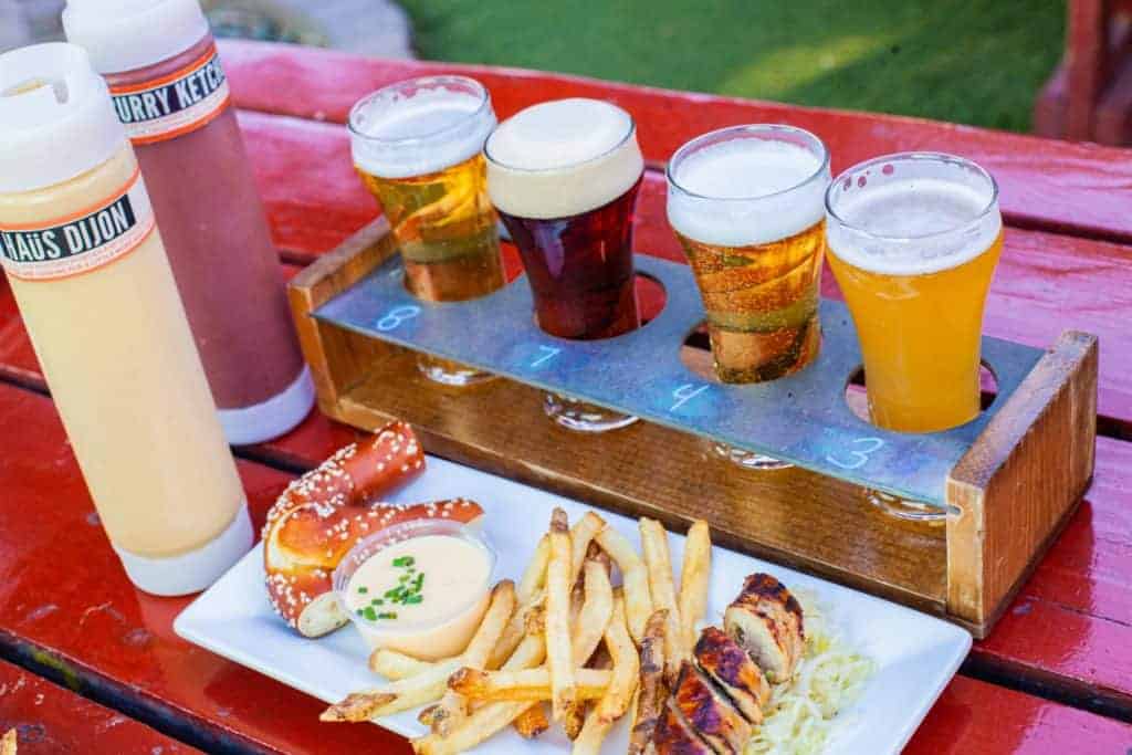 A wooden flight of four craft beers sits beside a plate foods