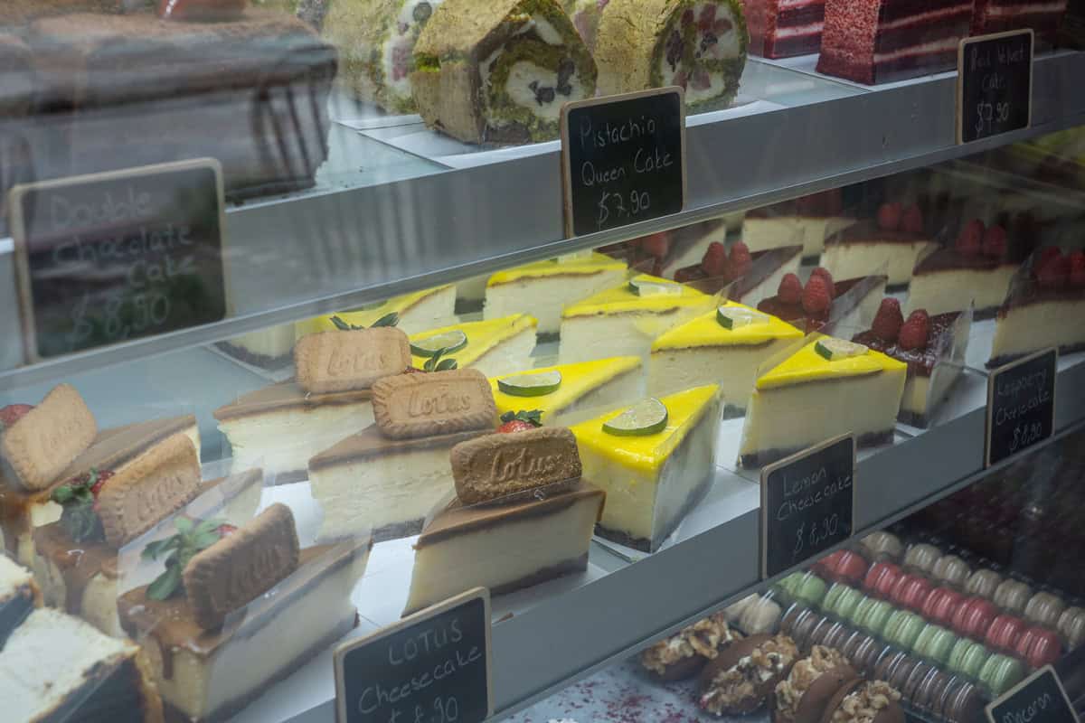A display case filled with various colorful cakes and cheesecakes at bake me happy in tomball