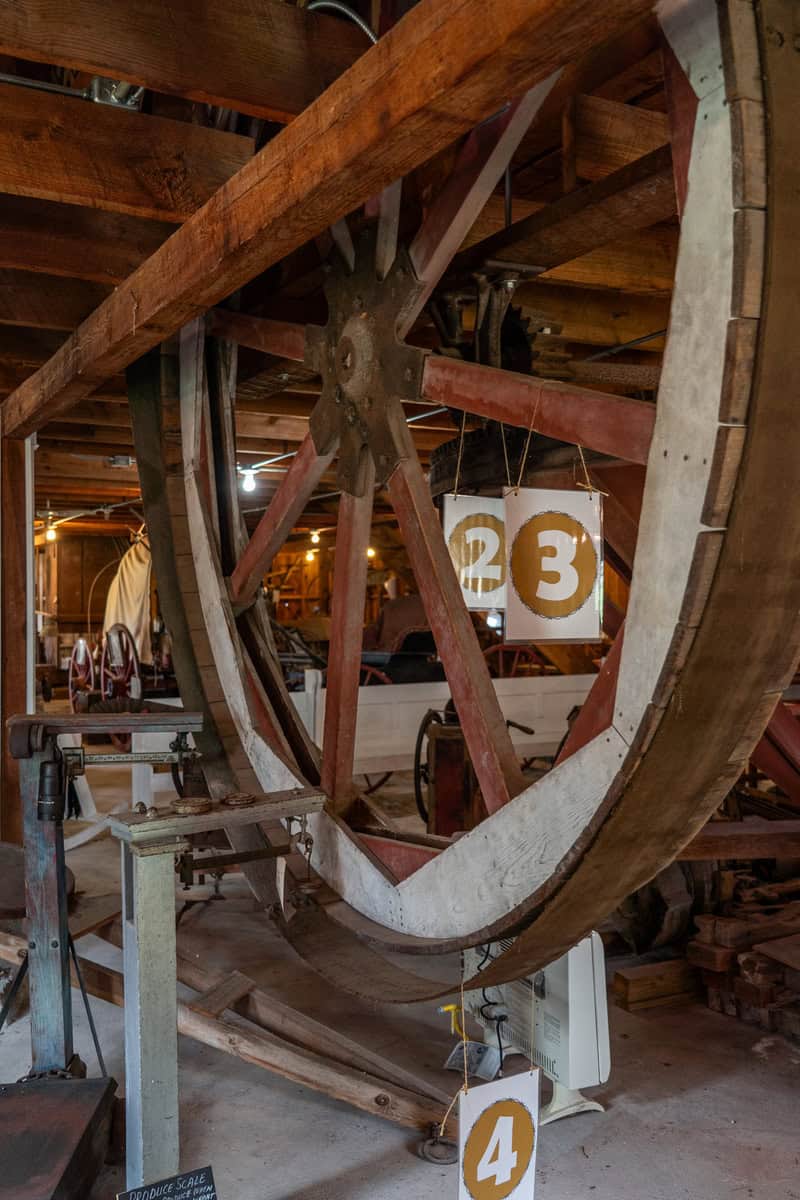 A large wooden wheel hangs in a rustic workshop, labeled with numbers 2, 3, and 4, in Tomball Museum Center
