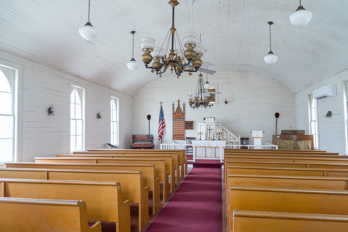 Interior of a quaint chapel with wooden pews, ornate chandeliers, a pulpit, and an American flag in Tomball Museum Center
