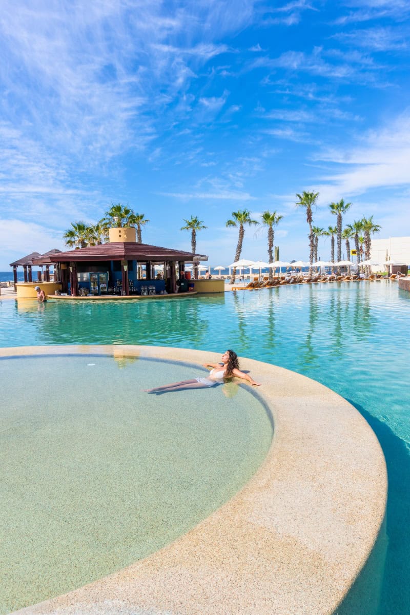 Relaxing woman floating on pool float at tropical resort with palm trees and clear blue sky.