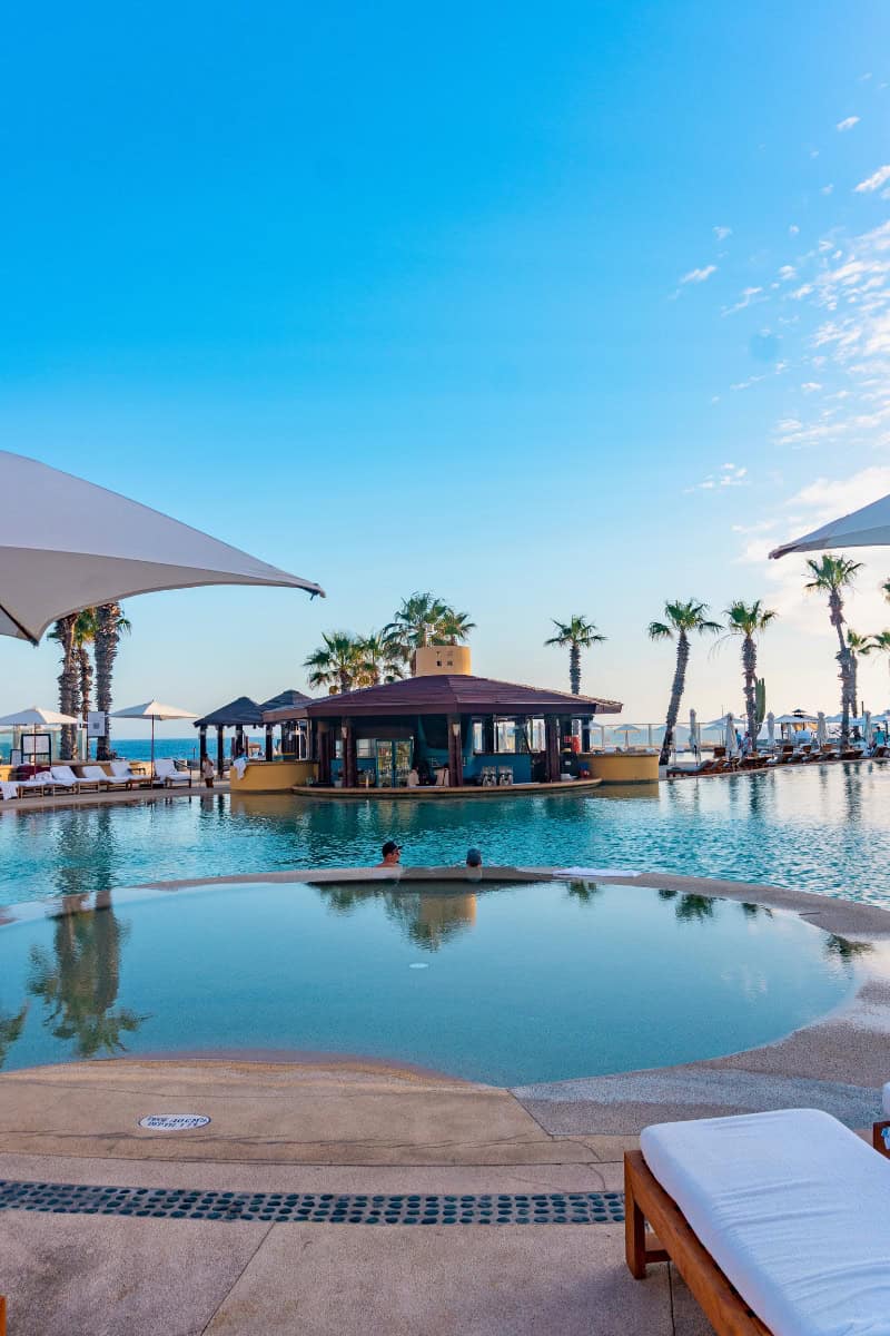 Relaxing poolside view at a tropical resort with palm trees and ocean in the background.