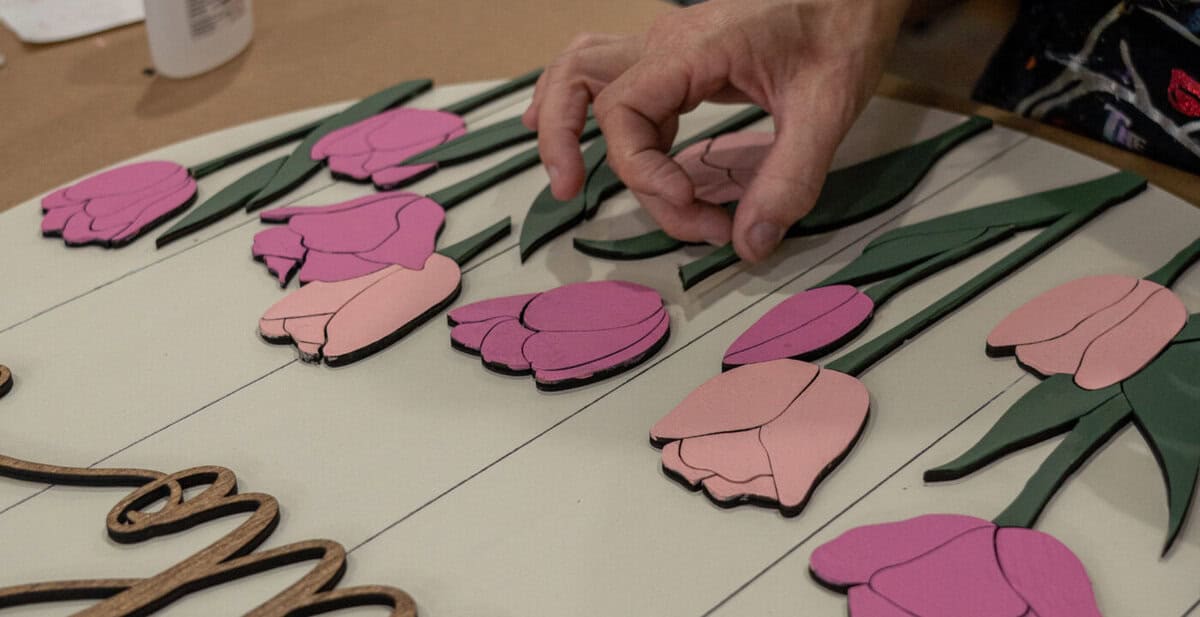 Hands arranging a floral wood craft project at Craft Chicks in Tomball